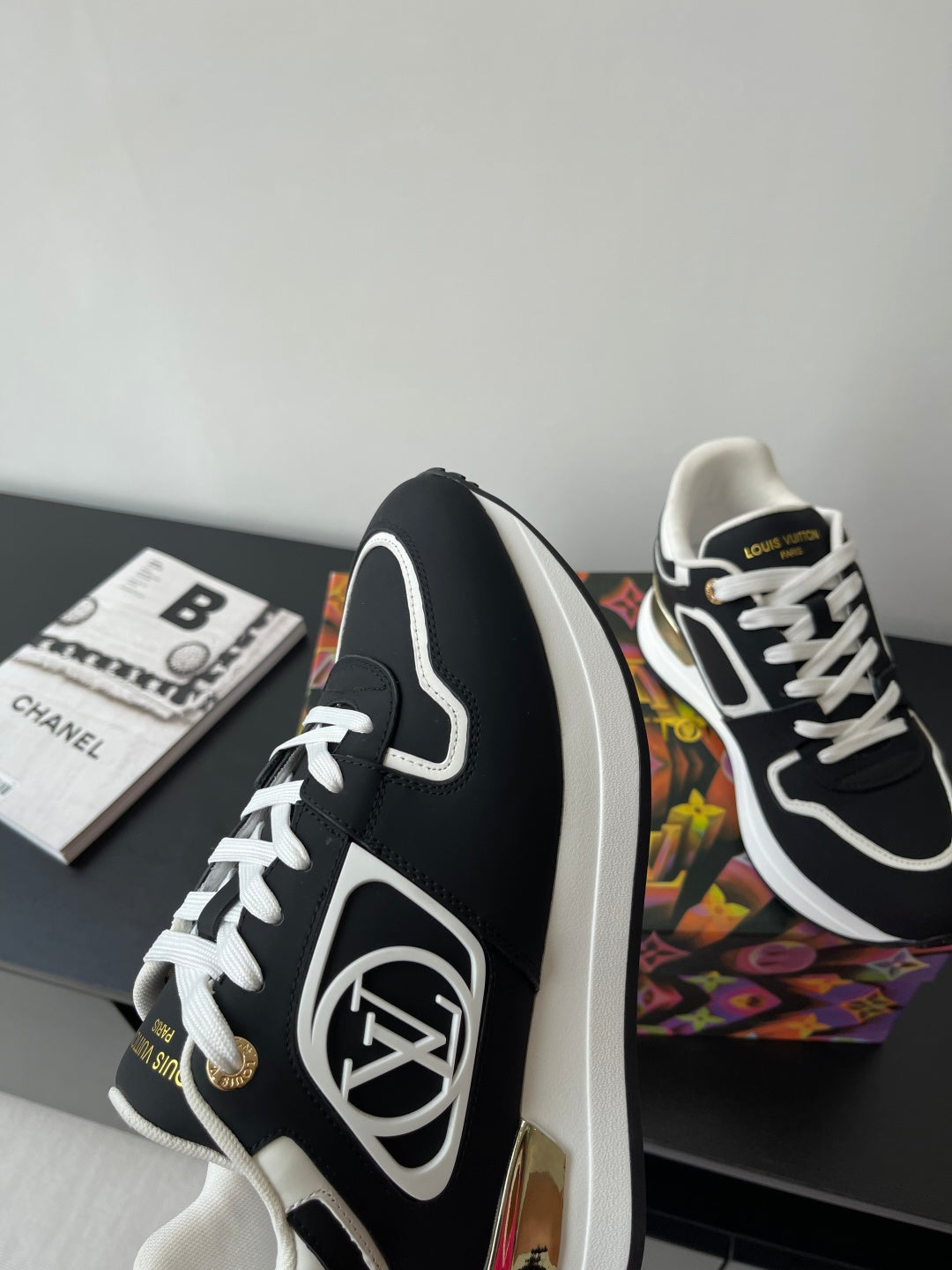 Ladies' Louis Vuitton sneakers side view, black leather look with white piping and gold emblem.
