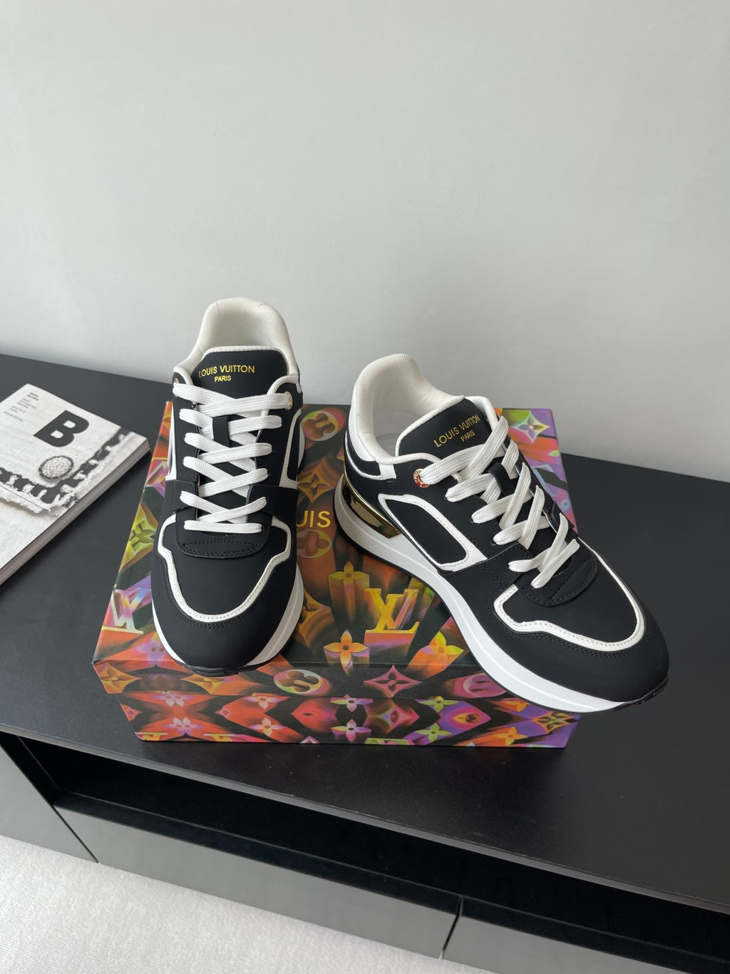 Ladies' Louis Vuitton sneakers, black and white with gold detailing on the side, angled view.
