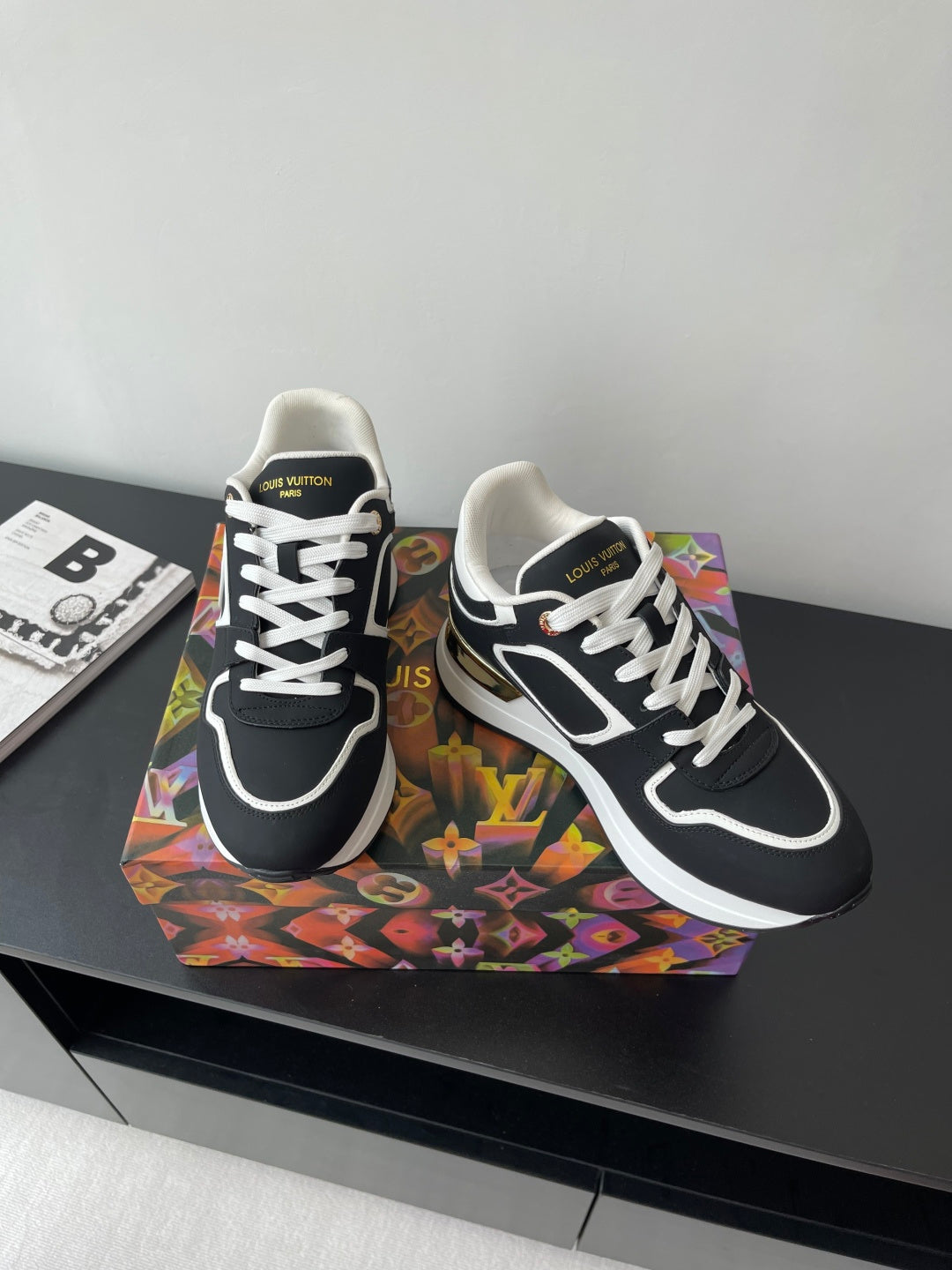 Ladies' Louis Vuitton sneakers, black and white with gold detailing on the side, angled view.
