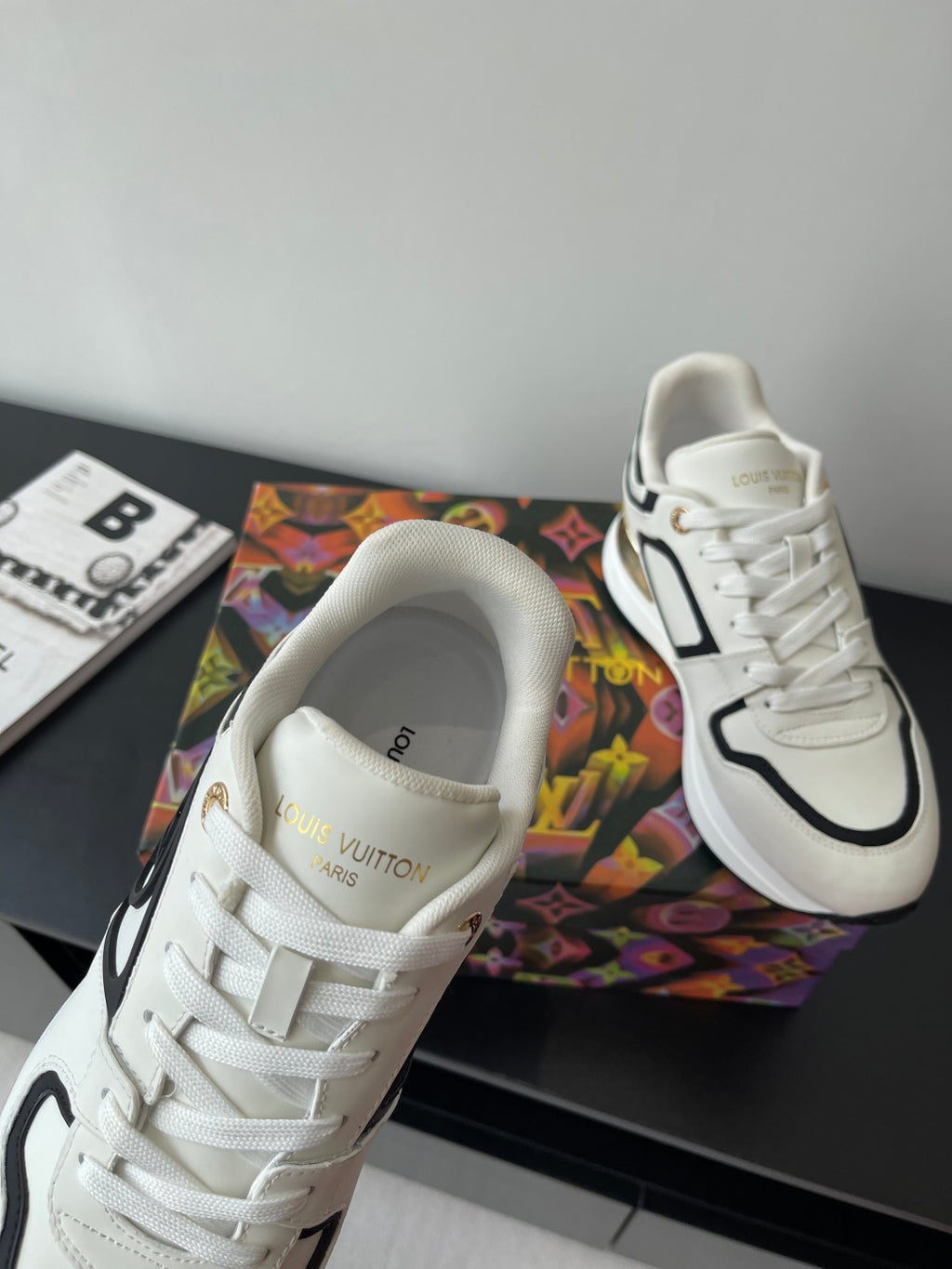 White Louis Vuitton sneaker with gold “LV” logo on the strap and black trim