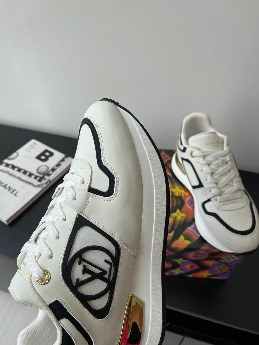 White Louis Vuitton sneakers with black trim and side emblem, on a box