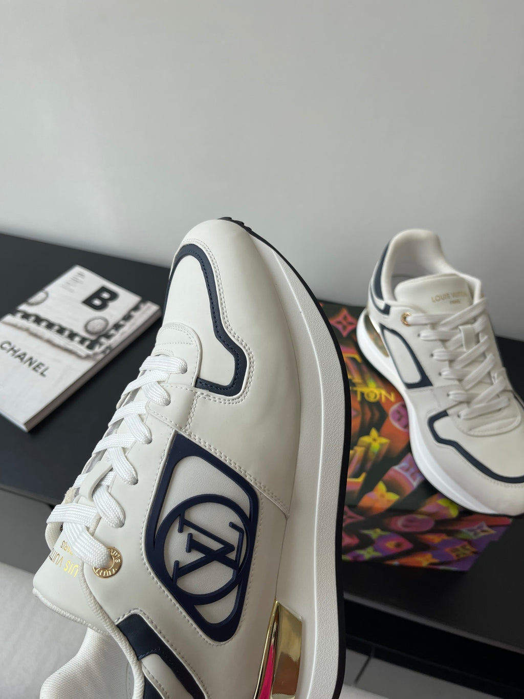 White low-top sneakers with navy side logo and gold lace aglet