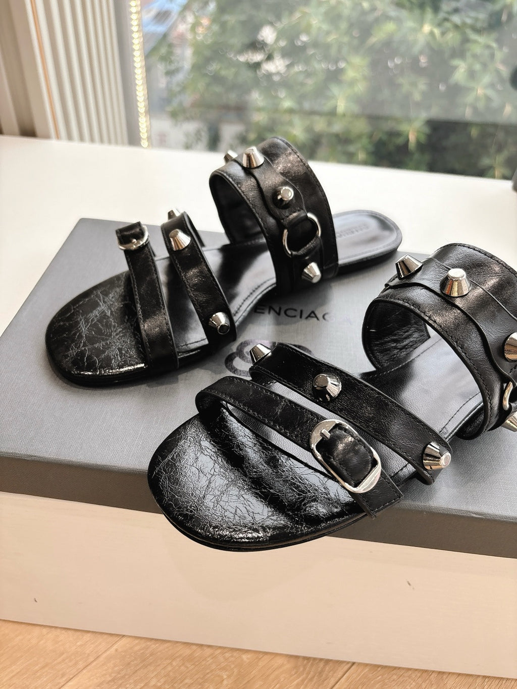 Black leather studded slide sandals with silver buckles and open toe on box