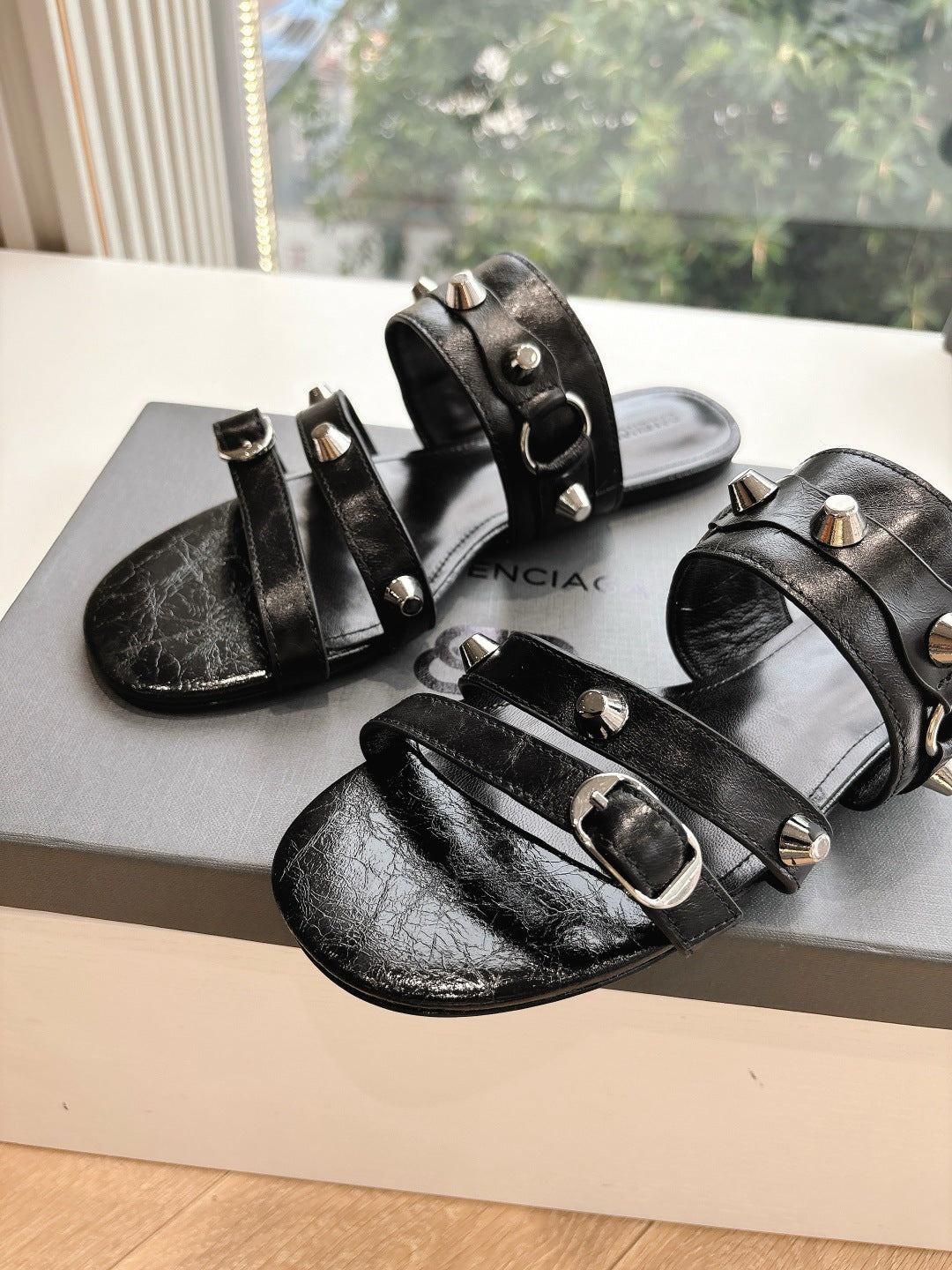 Black leather studded slide sandals with silver buckles and open toe on box