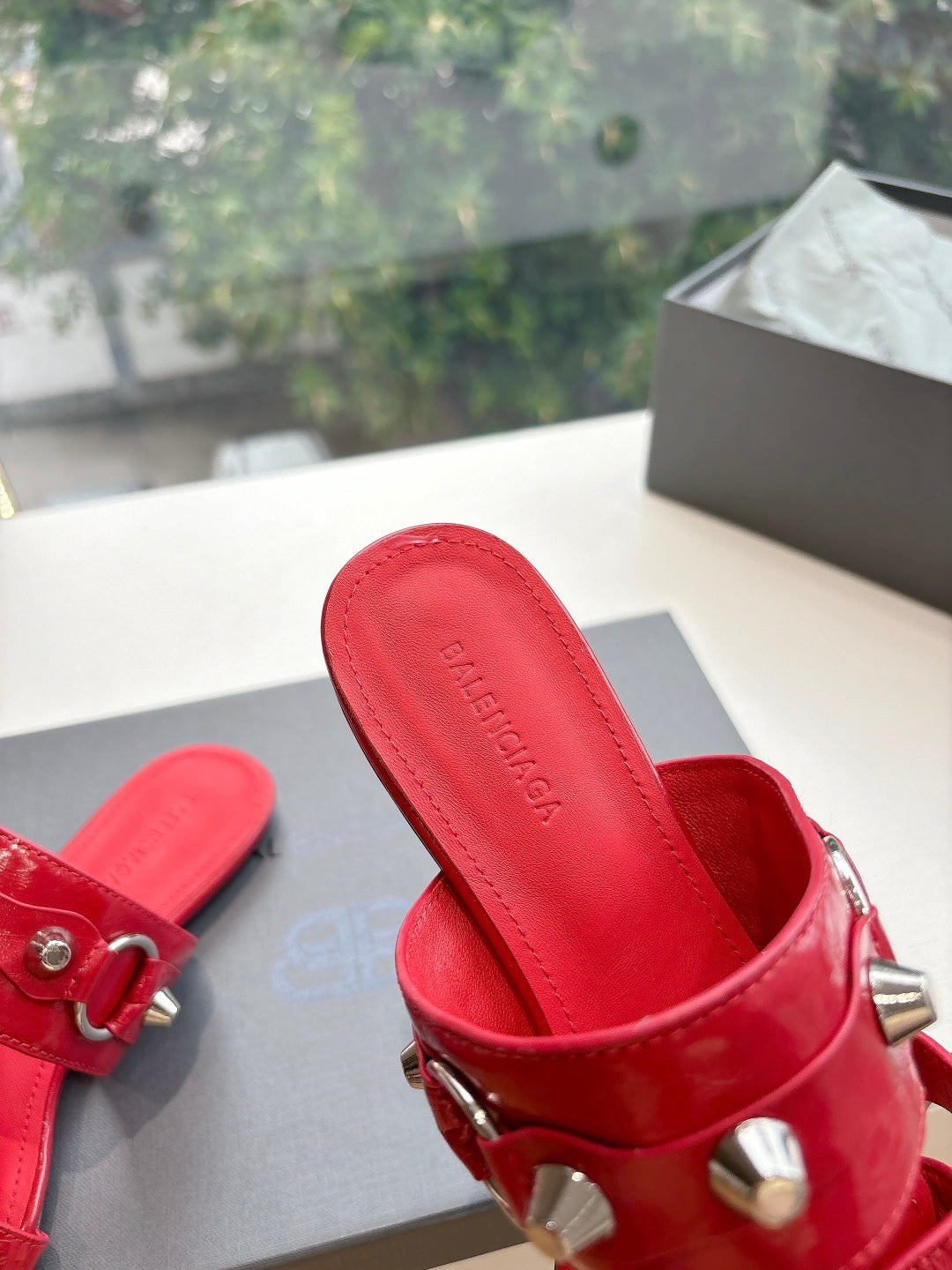 Red slide sandal with silver studs, buckle strap, and Balenciaga logo on footbed