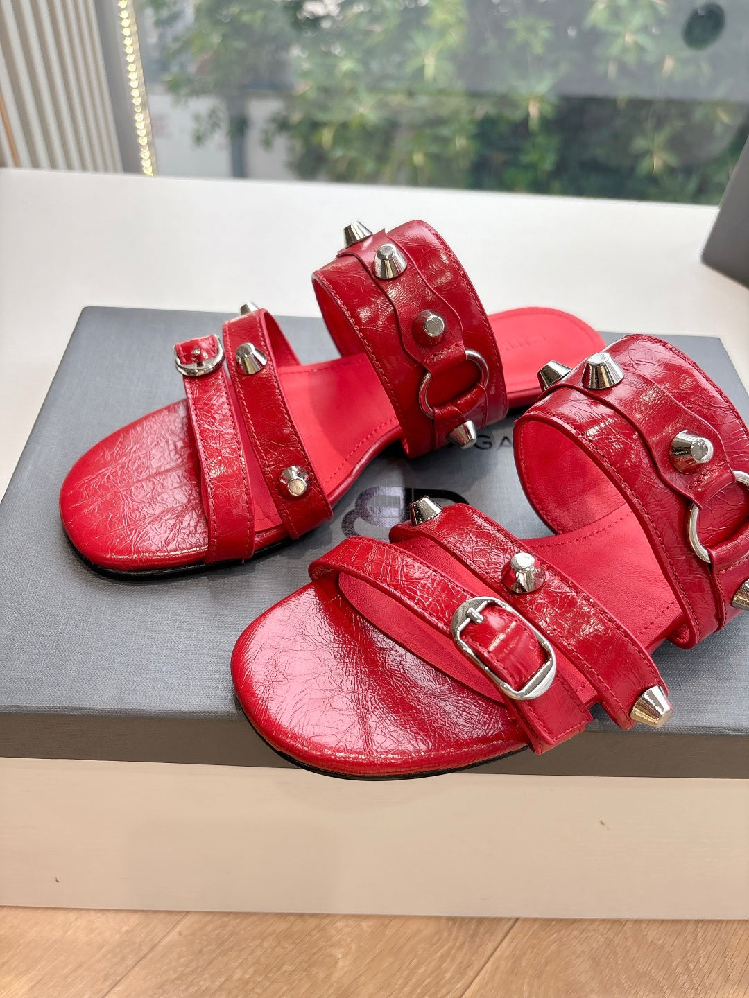 Red leather-like slide sandals with silver studs and buckled straps