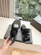 Black leather slide sandals with buckled straps and tag on the box