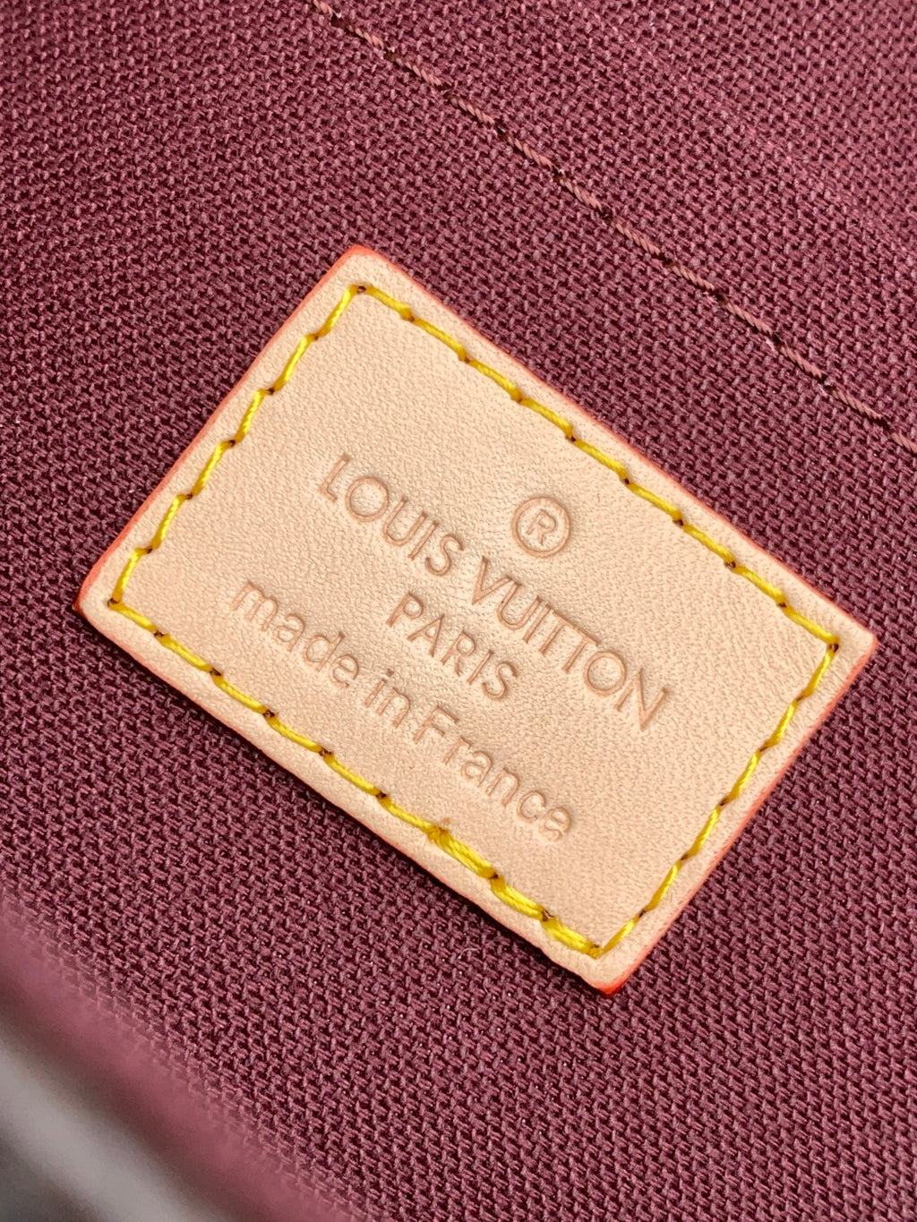 Louis Vuitton brand label tag on maroon fabric, stitched edges, Made in Paris, France.