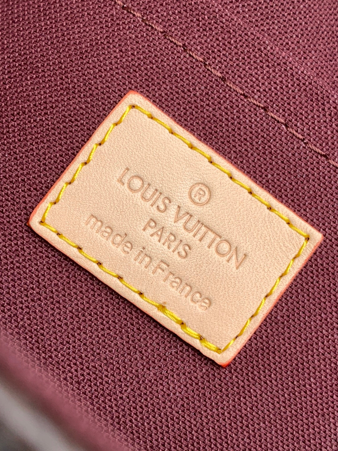 Louis Vuitton brand label tag on maroon fabric, stitched edges, Made in Paris, France.