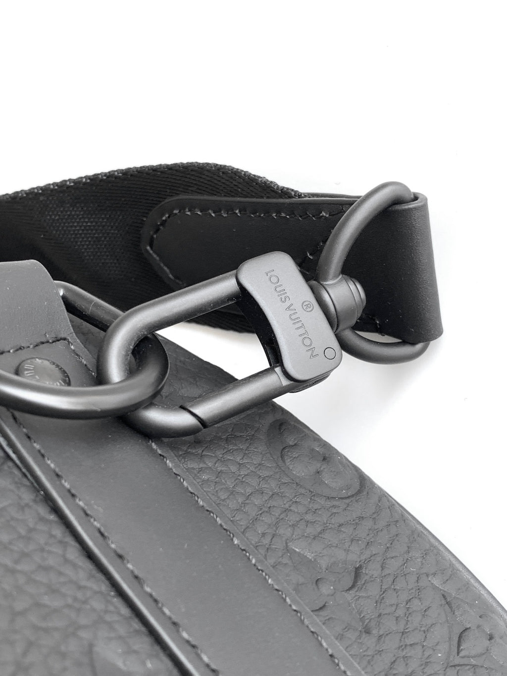 Louis Vuitton monogram strap and metal D-rings on black leather bag.