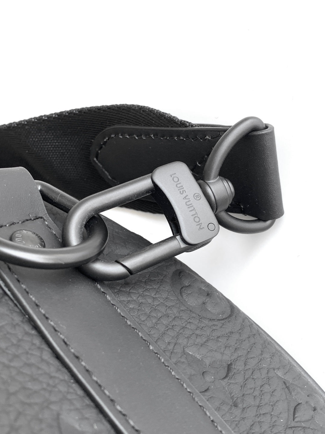 Louis Vuitton monogram strap and metal D-rings on black leather bag.