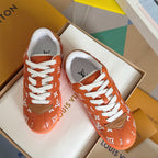 Orange monogram sneakers with white laces and tan patch detail, pair on box