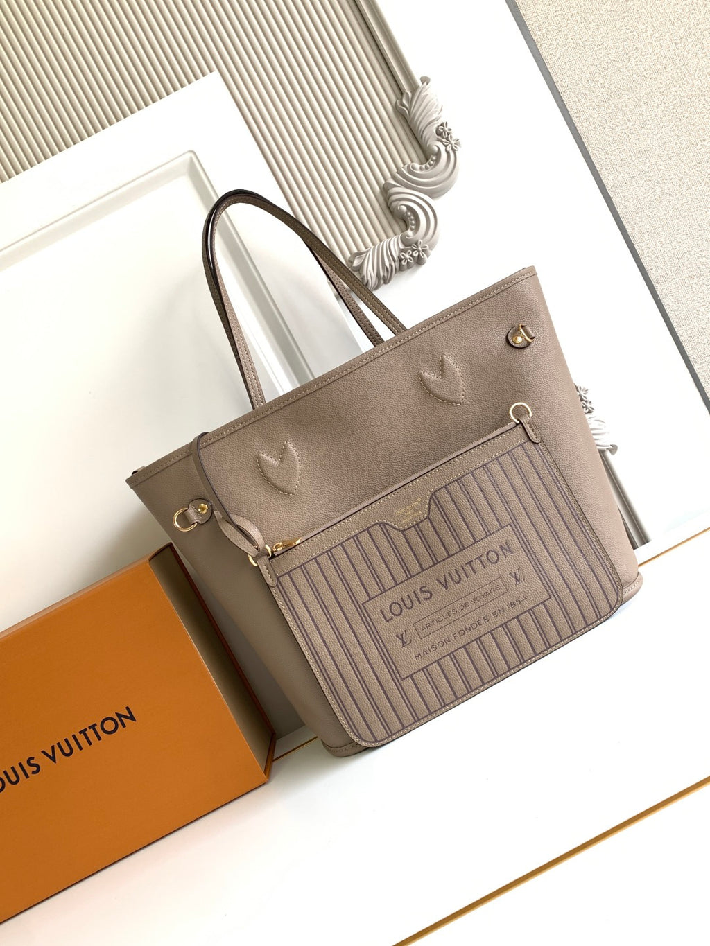 Beige monogram tote bag with light striped front panel, top handles, and gold hardware