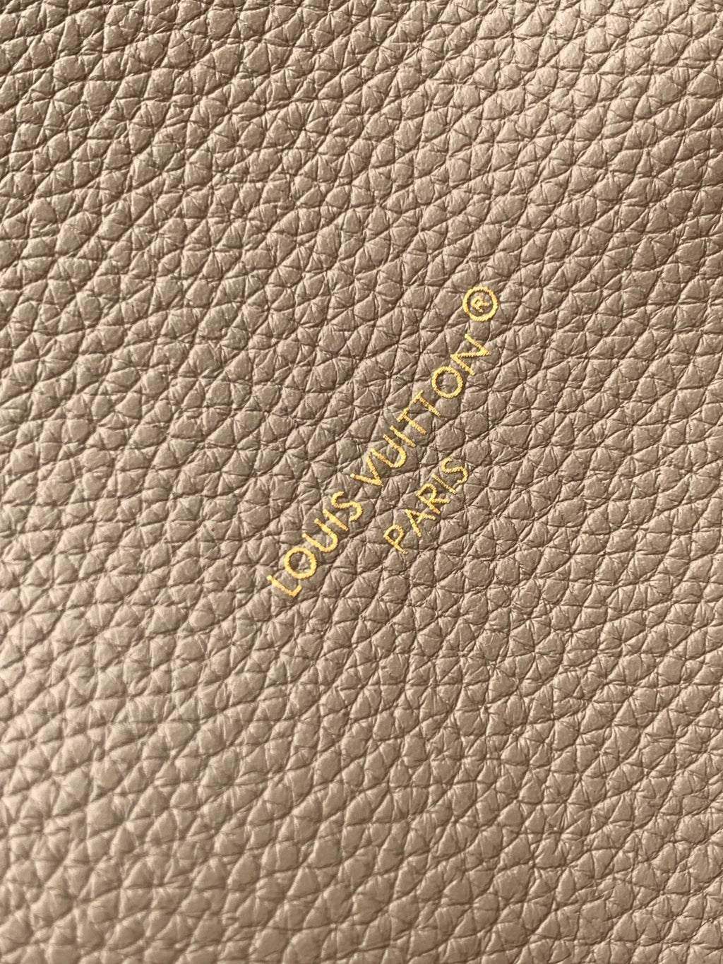 Beige textured leather fabric with small embossed logo and gold-toned accents