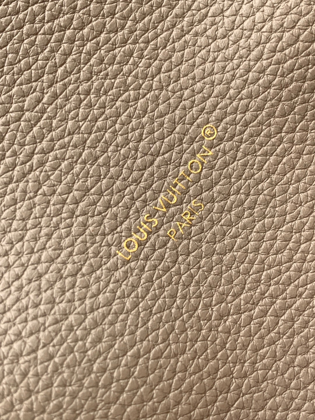 Beige textured leather fabric with small embossed logo and gold-toned accents