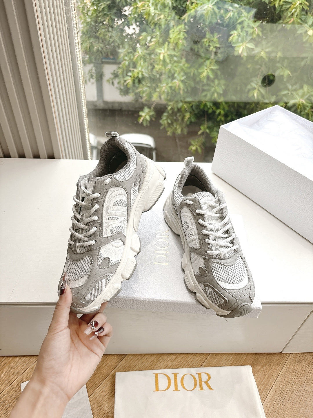 Women’s lace-up sneakers held up, light gray and white, on a white display box