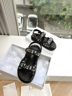 Pair of black Dior sandals with patterned front straps and adjustable buckle
