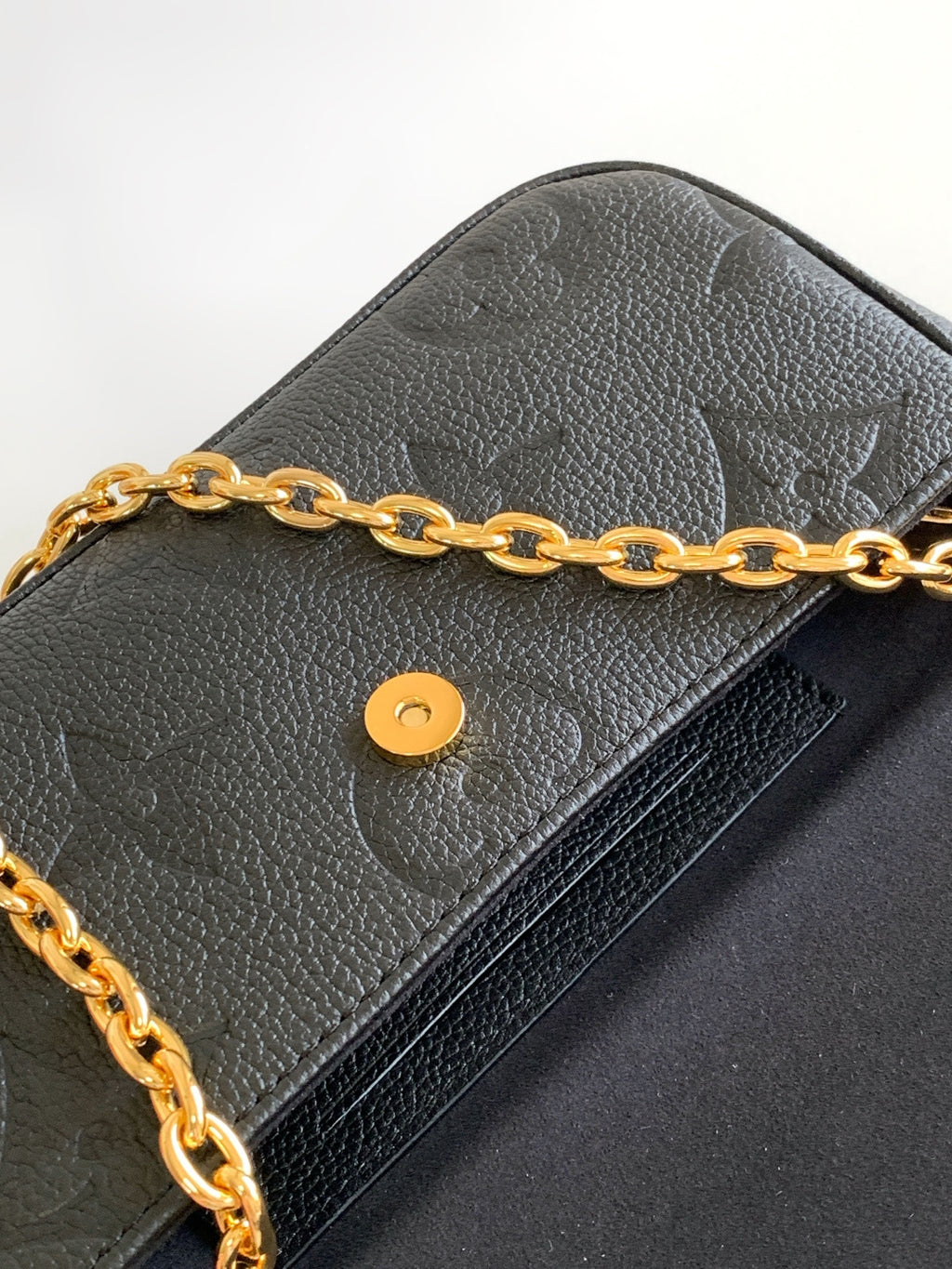 Close-up of black leather flap bag with gold chain and round snap button