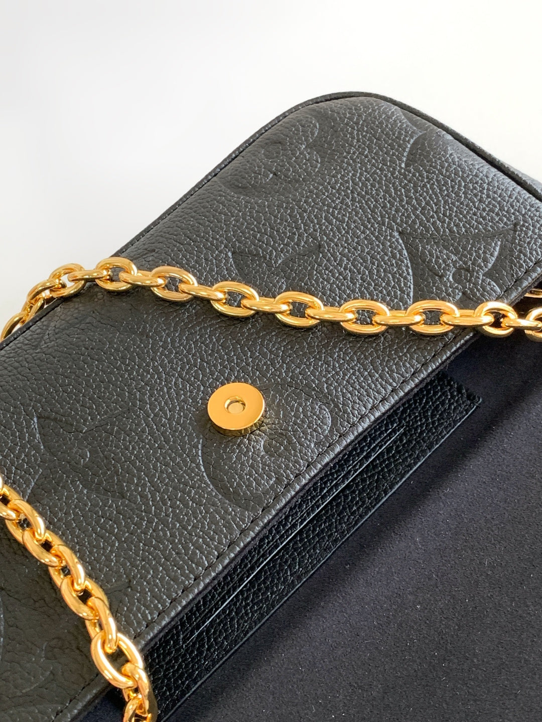 Close-up of black leather flap bag with gold chain and round snap button