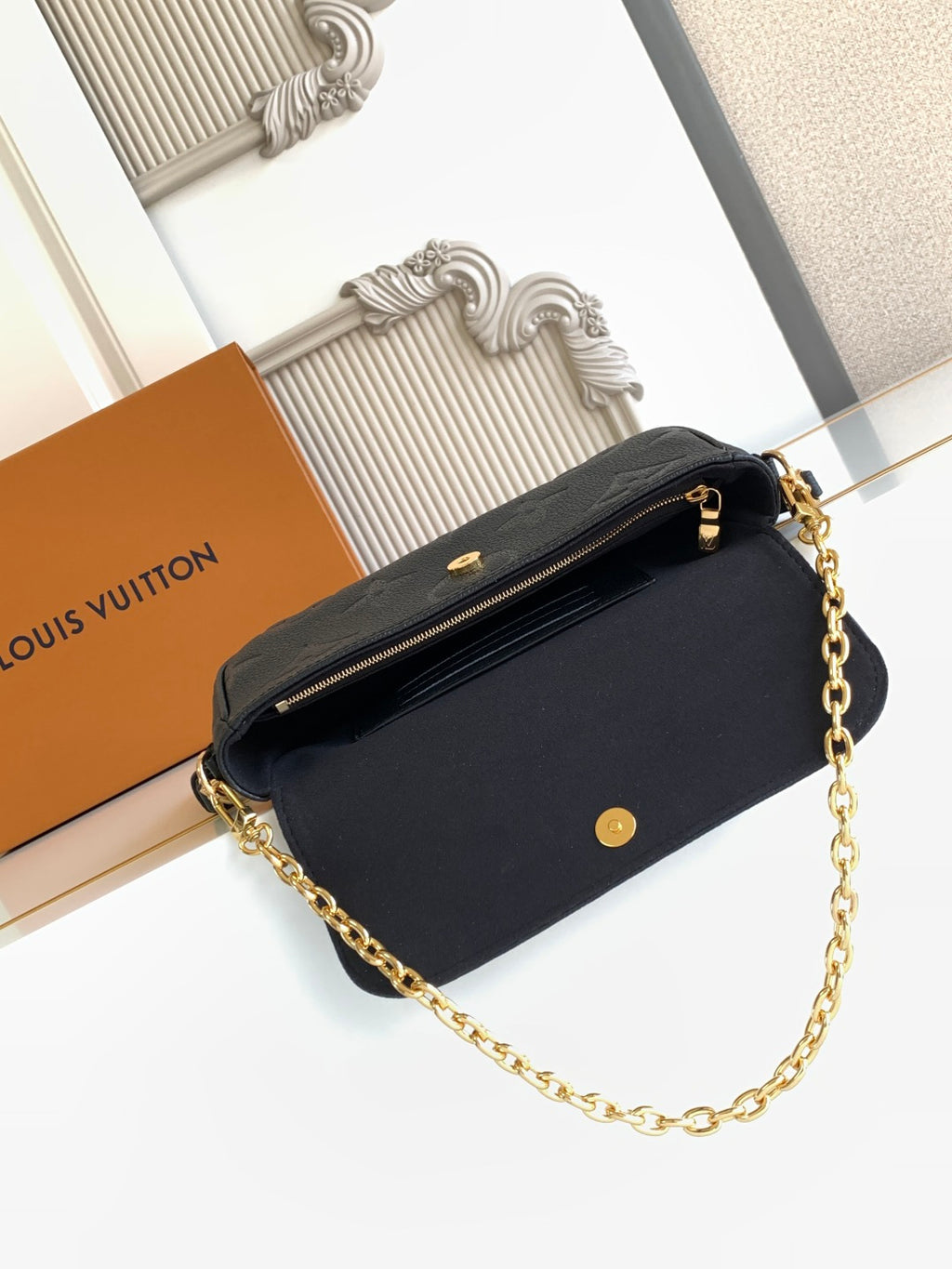 Black leather shoulder bag with gold chain strap, front snap button, and top zip