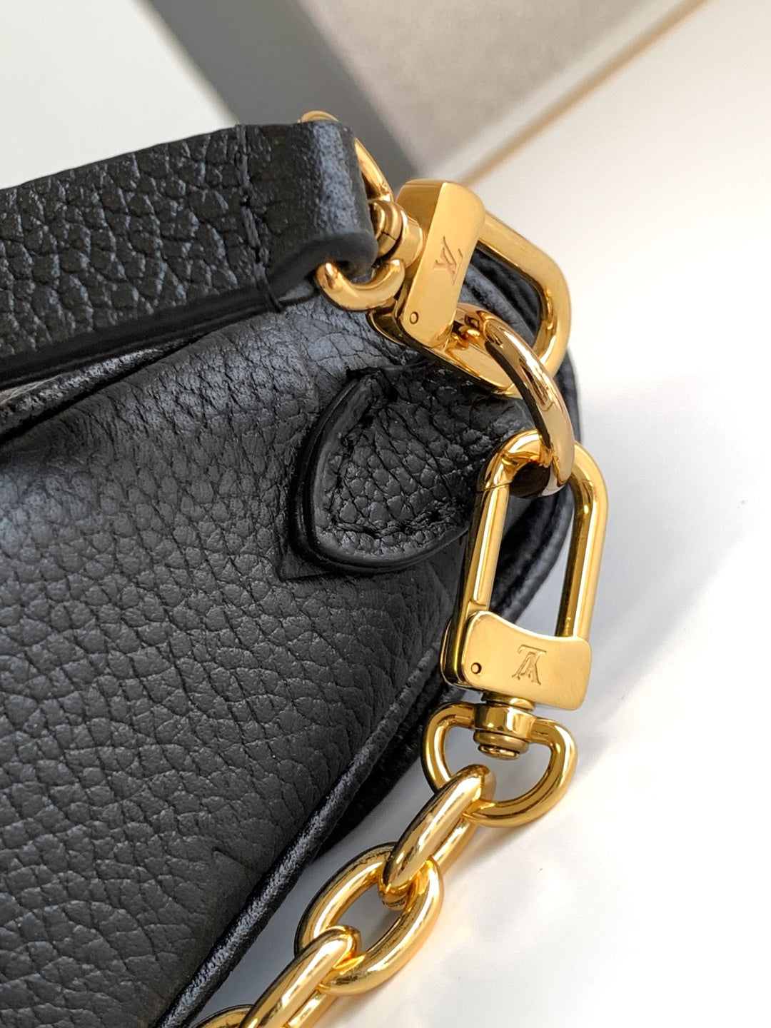 Close-up of black leather bag clasp with gold hardware and chain strap