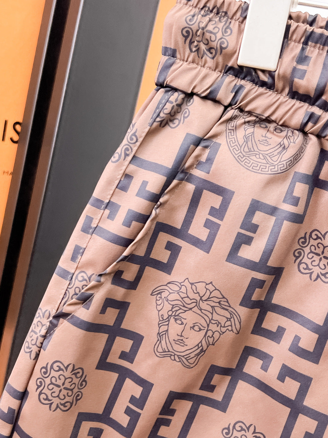 Logo-pattern shorts detail: elastic waistband and large Medusa-style graphic, tan with navy