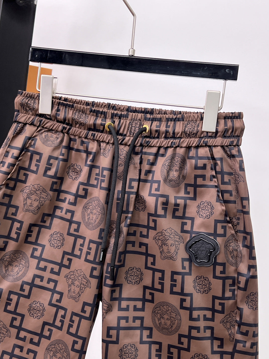 Logo-pattern shorts front view with black medallion patch on tan fabric and navy print