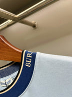 Burberry navy-and-cream logo trim at T-shirt neckline on light blue fabric.