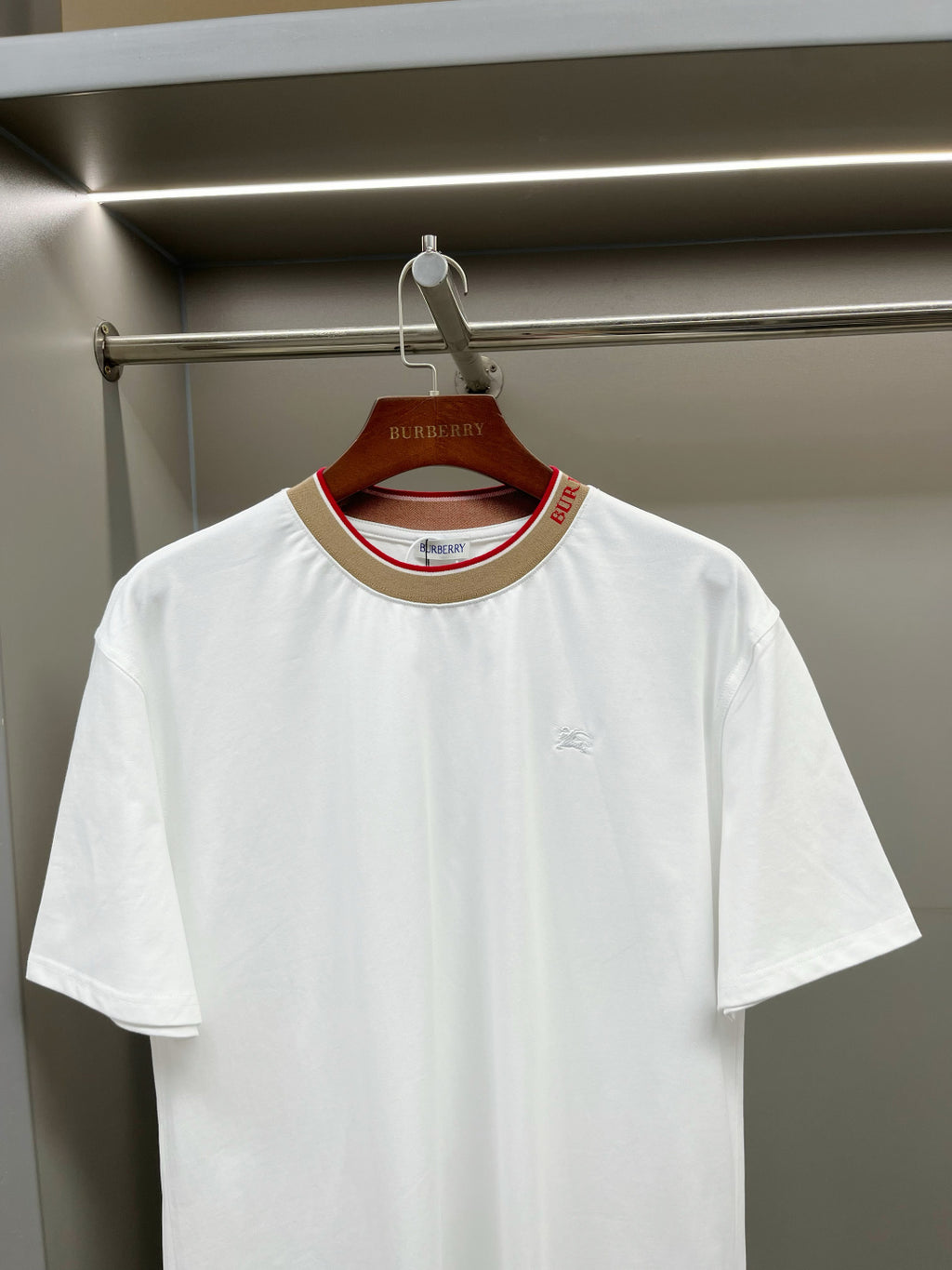 White short-sleeve T-shirt with tan collar and red trim, front chest logo detail.