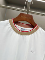 White crew-neck T-shirt with tan trim and red/green striped collar lining; Burberry logo.