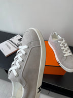 Hermes ladies sneakers side view, light gray with white laces on an orange box