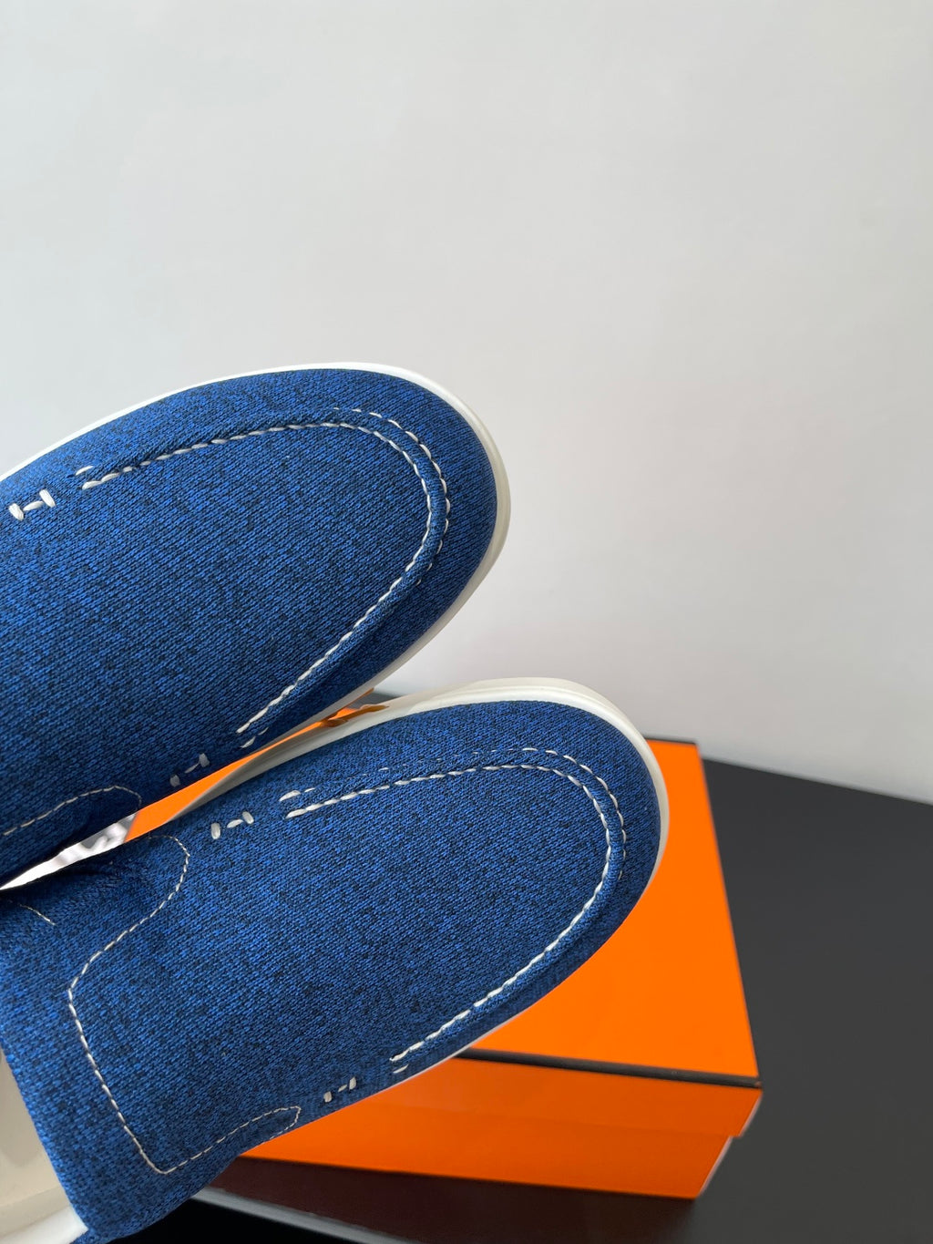 Close-up of blue denim slip-on shoes with white stitching and curved toe seam.