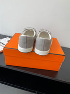Hermes back view of light gray slip-on sneakers with heel pull tabs, white soles