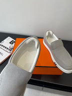 Hermes light gray canvas slip-on sneakers, interior lining visible, white rubber sole
