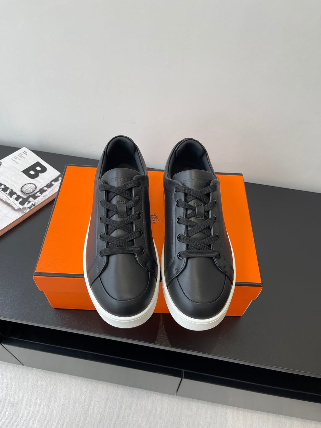 Low-top leather sneakers, black lace-up with white rubber sole, placed on orange box.