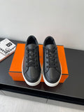 Low-top leather sneakers, black lace-up with white rubber sole, placed on orange box.