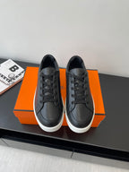 Low-top leather sneakers, black lace-up with white rubber sole, placed on orange box.