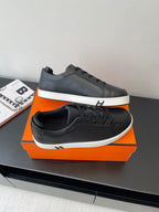 Pair of black low-top sneakers with lace-up front and white rubber sole, on orange box.