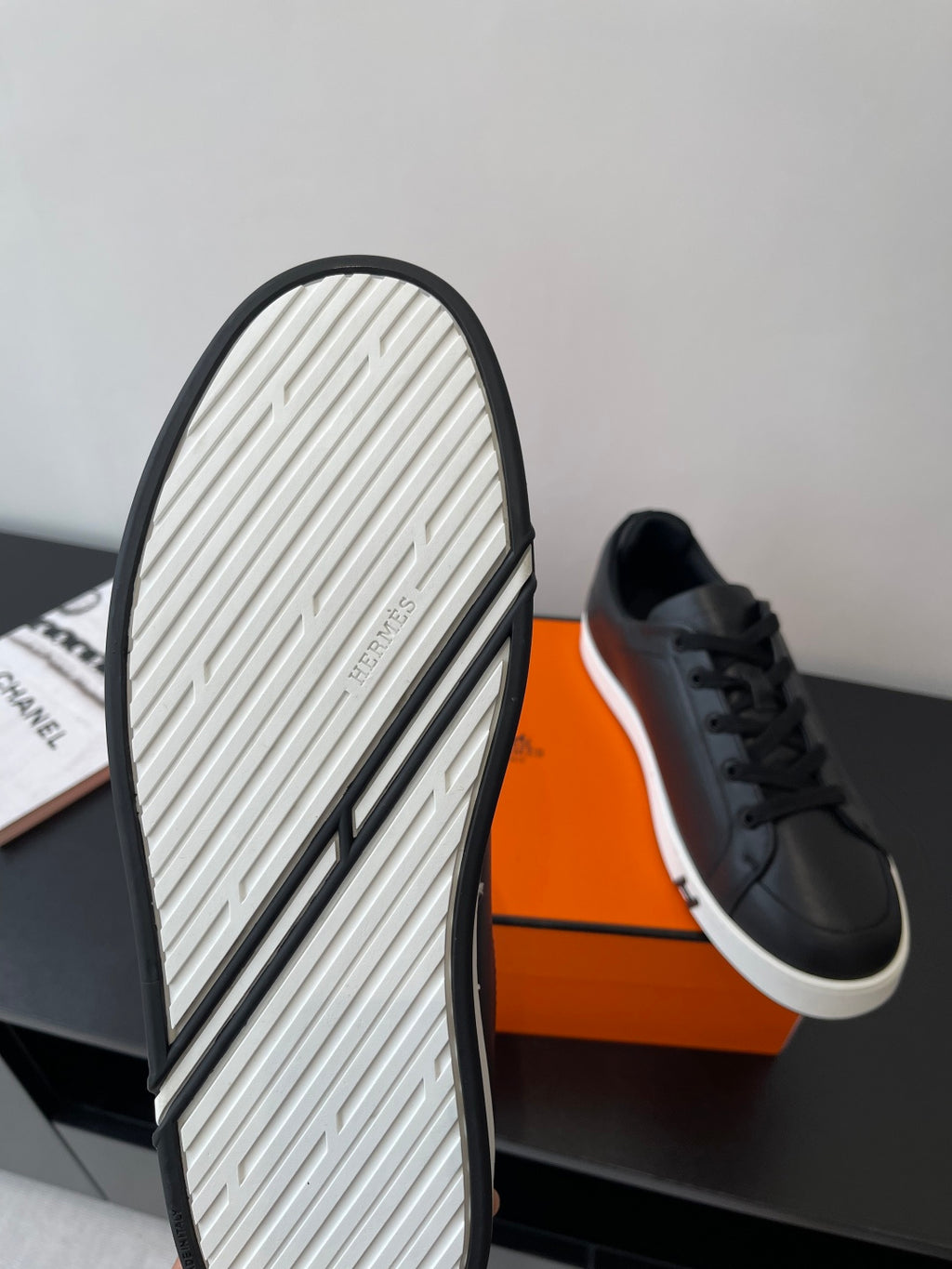 Sneaker outsole view with black rubber edge and textured tread, with black shoe above.