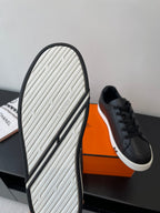 Sneaker outsole view with black rubber edge and textured tread, with black shoe above.