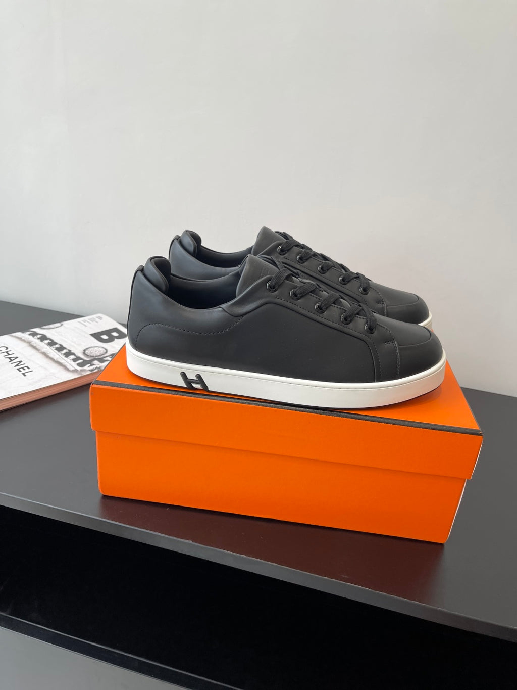 Low-top sneakers in black leather with lace-up front and white sole edge on orange box.