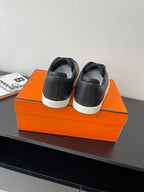 Rear view of black low-top sneakers with lace-up tops and white rubber sole, on orange box.