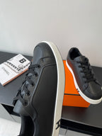 Black leather low-top sneakers with lace-up front and white sole trim, side view.