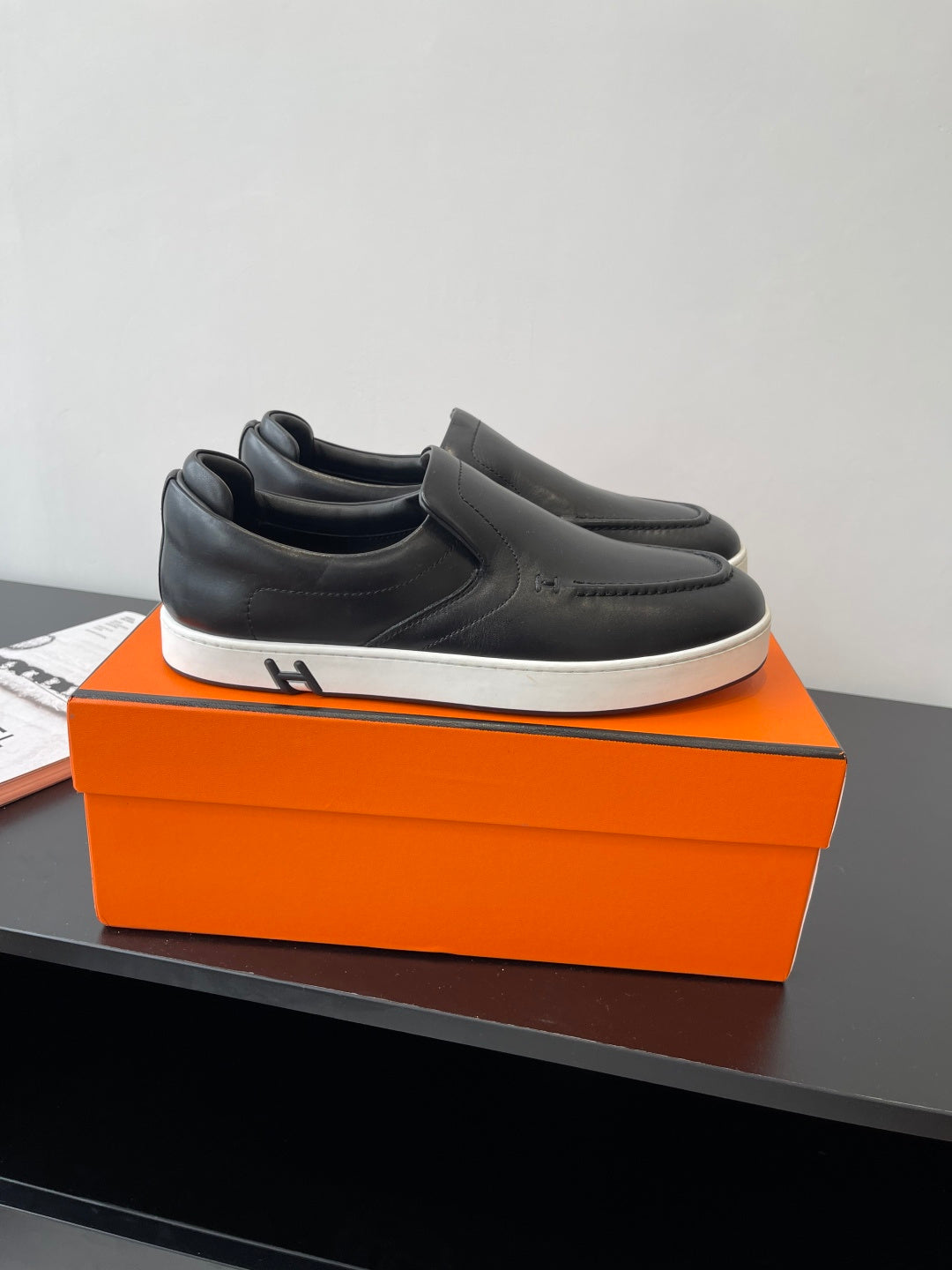 Black leather slip-on loafers on orange shoebox, low-profile white sole