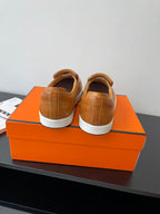Back view of brown slip-on loafers with white soles on top of orange box.