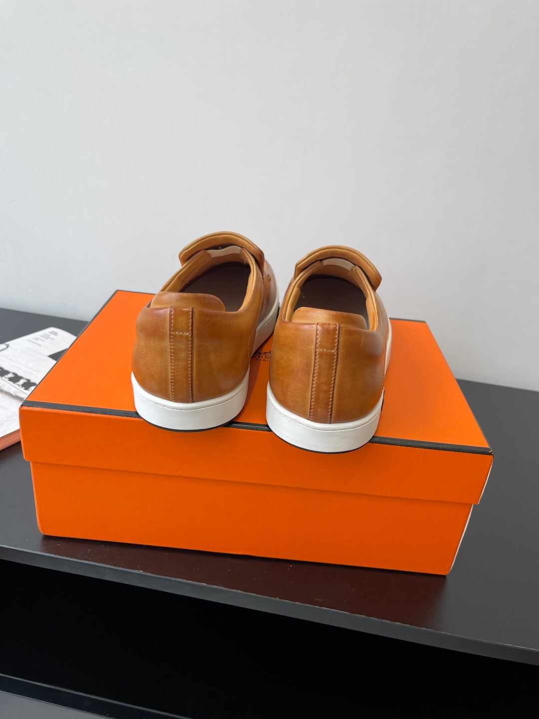 Back view of brown slip-on loafers with white soles on top of orange box.