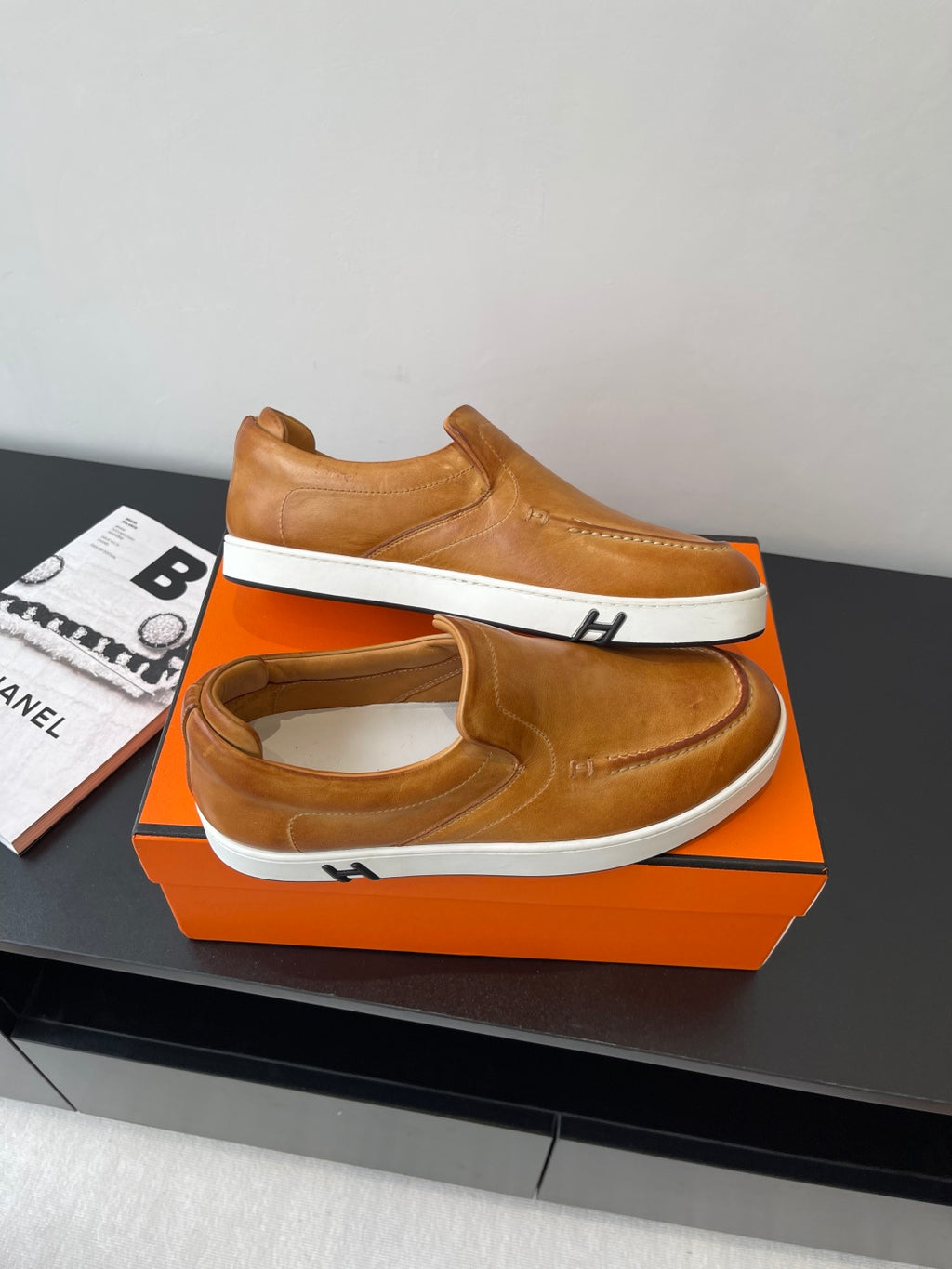Angled view of brown slip-on loafers with white soles and signature-style stitched detail.