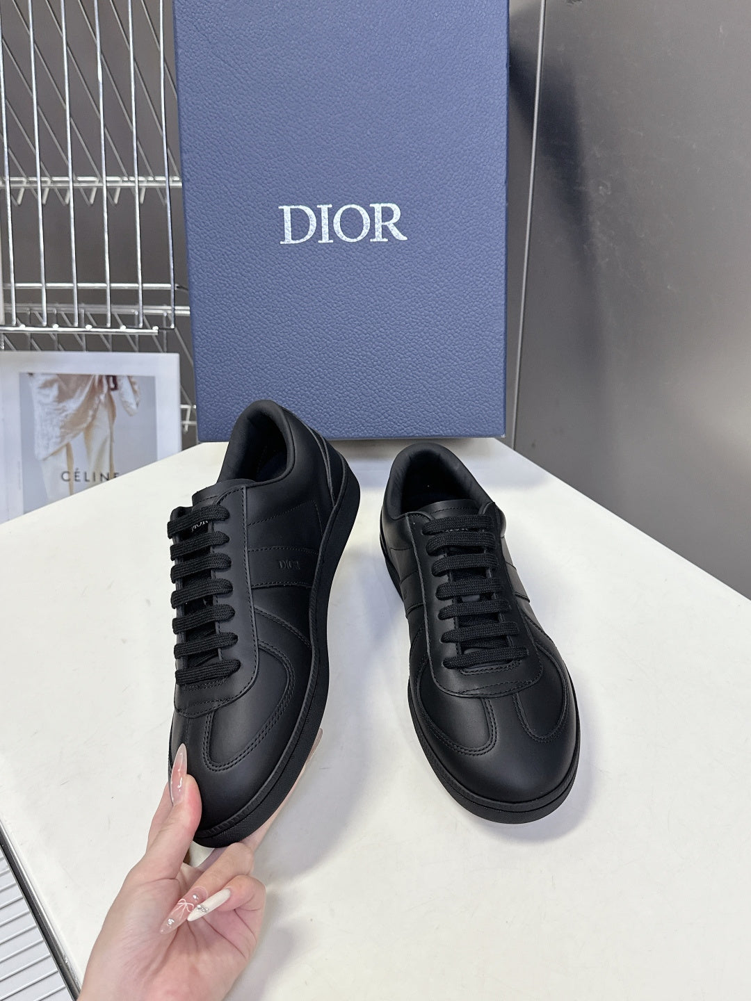 Black lace-up sneakers pair held by hand, low-profile cup sole