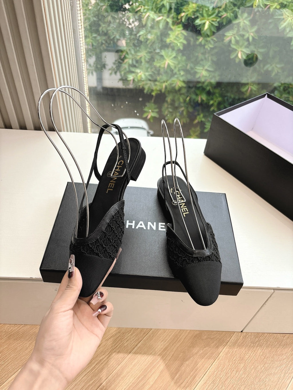 Black Chanel women's slingback shoes with long ankle straps, held in hand beside box