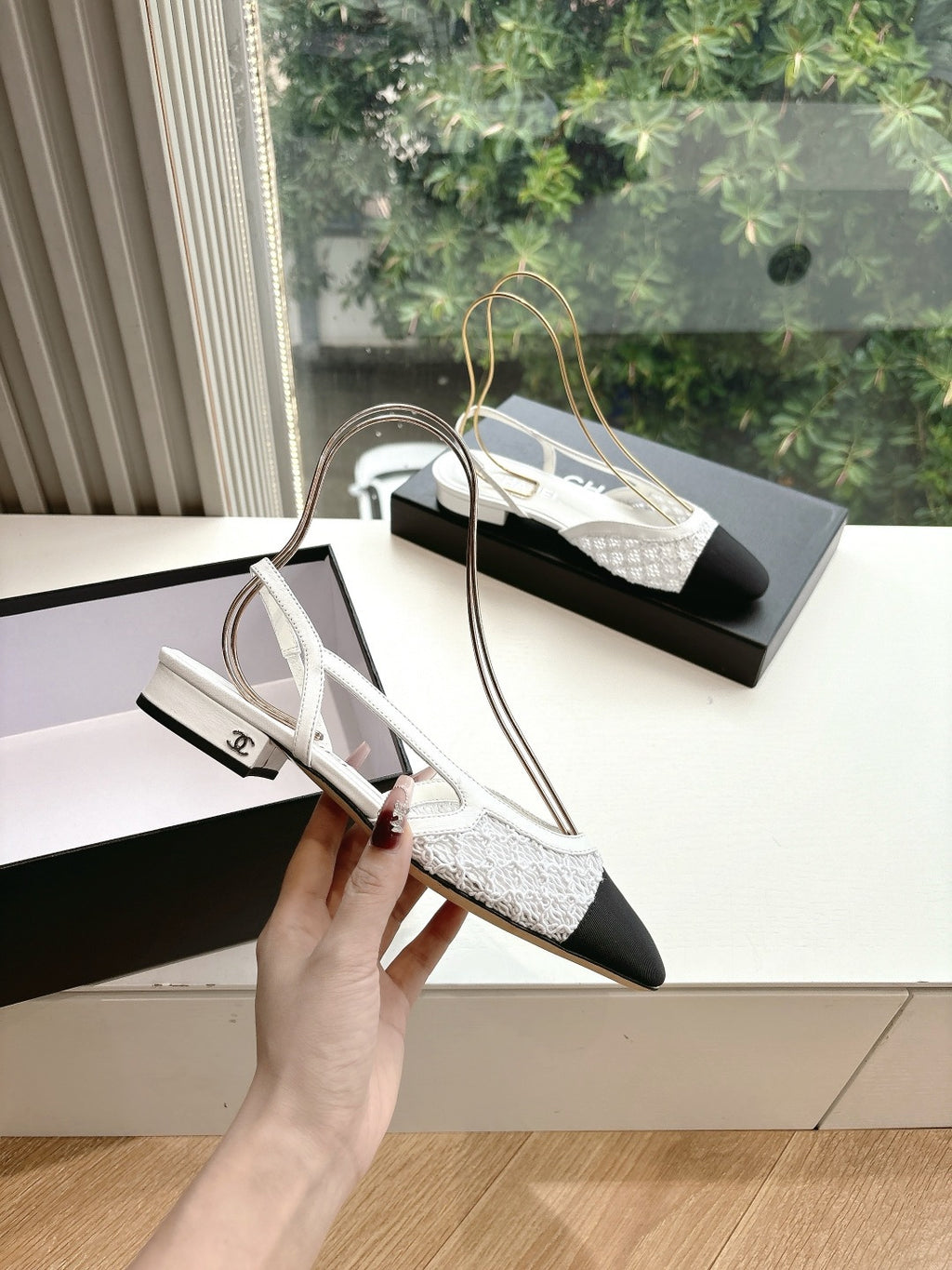 Chanel ladies slingback pump, white textured upper with black toe and heel, held in hand